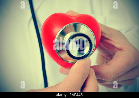 Un medico auscultating un cuore rosso con uno stetoscopio, con un effetto retrò Foto Stock