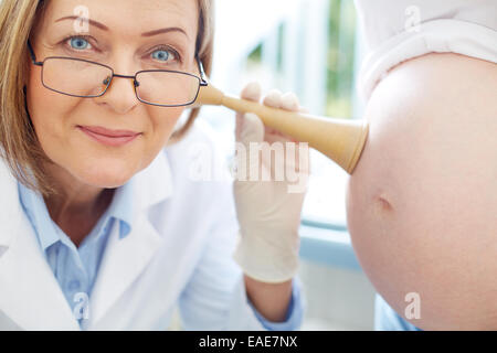 Ginecologo maturo esame il battito del cuore del bambino nel ventre femminile Foto Stock