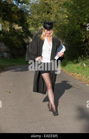 Studenti maturi che indossa il cappello e camice in possesso di un libro di riferimento a piedi in strada Foto Stock