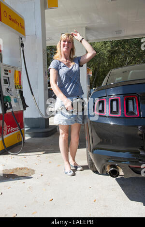 Donna automobilista in corrispondenza di una stazione di gas di riempimento di un nero Ford Mustang auto sportiva NEGLI STATI UNITI Foto Stock