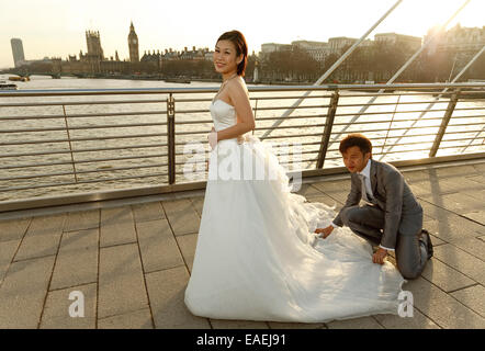 Un East Asian sposa ha il suo abito da sposa disposti dal suo Sposo nella parte anteriore del paesaggio di Londra e Westminster - retroilluminati da Sun Foto Stock