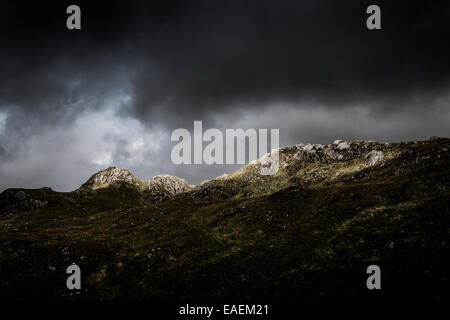 Un breve raggio di sole si rompe in un cielo tempestoso e colpisce una collina Foto Stock