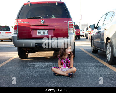 Una giovane ragazza in un abito colorato si siede in un parcheggio e attende Foto Stock