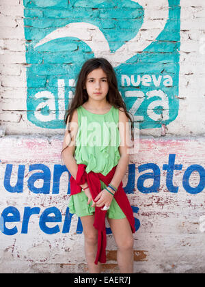Ritratto di giovane ragazza in Messico si erge di fronte a un muro di mattoni dipinto con gli annunci pubblicitari Foto Stock