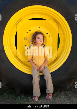 Giovane ragazza seduta sulla grande giallo carrello ruota e lo sguardo lontano pensively Foto Stock