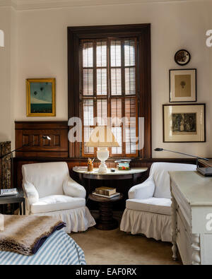 Coppia di divani profondi con cotone scivola fiancheggianti una tabella demilune in camera con finestra originale otturatori Foto Stock