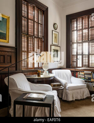 Coppia di divani profondi con cotone scivola fiancheggianti una tabella demilune in camera con finestra originale otturatori Foto Stock