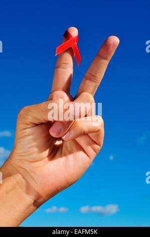 Un man mano che il segno V con un rosso nastro di sensibilizzazione per la lotta contro l AIDS Foto Stock