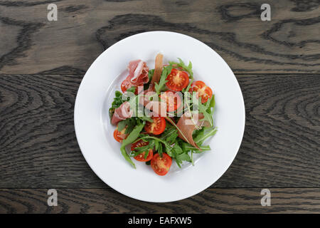 Con insalata di rucola prosciutto e pomodoro, sul tavolo di legno Foto Stock