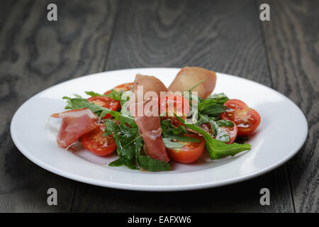 Con insalata di rucola prosciutto e pomodoro, sul tavolo di legno Foto Stock