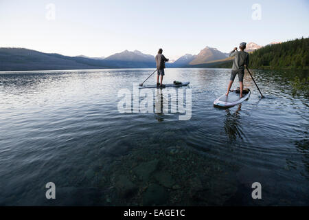 Un uomo e una donna stand up paddle boards (SUP) sul Lago McDonald nel Glacier National Park. Foto Stock