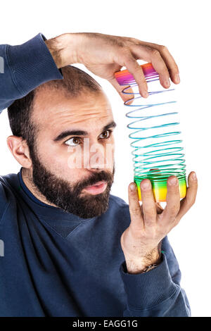 Un uomo barbuto giocando con un arcobaleno slinky giocattolo e cercando silly Foto Stock