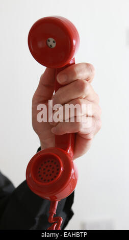 Mano d'uomo in possesso di un vecchio telefono rosso. Foto Stock