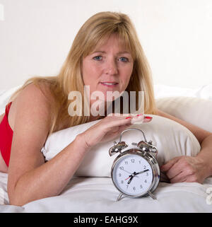 La donna posa in letto con un orologio di allarme Foto Stock