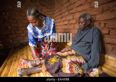 Una donna si prende cura di un anziano malato a casa nel distretto di Mulanje, Malawi. Foto Stock