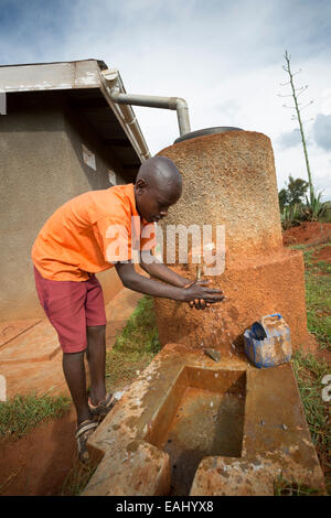 Uno studente si lava le mani al di fuori i boys' blocco servizi igienici a Kaptomologon scuola primaria a Bukwo, Uganda utilizzando acqua da una rai Foto Stock