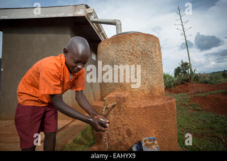 Uno studente si lava le mani al di fuori i boys' blocco servizi igienici a Kaptomologon scuola primaria a Bukwo, Uganda utilizzando acqua da una rai Foto Stock