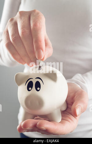 Donna mettendo coin in piggy coin bank, messa a fuoco selettiva con profondità di campo Foto Stock