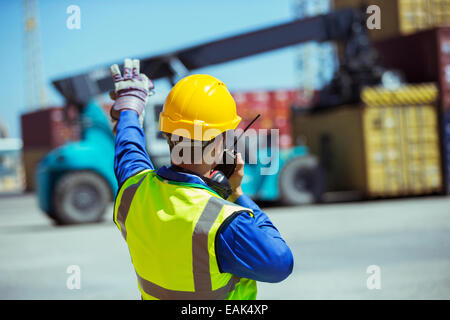 Lavoratore utilizzando un walkie-talkie vicino ai contenitori di carico Foto Stock