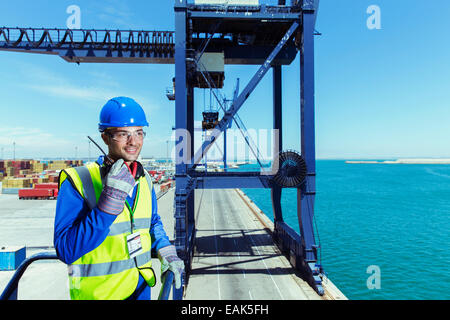 Lavoratore utilizzando un walkie-talkie sul carico gru a waterfront Foto Stock