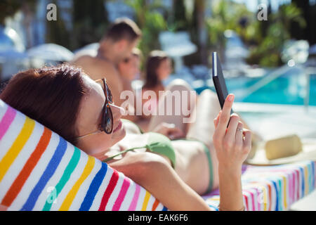 La donna a prendere il sole e i messaggi di testo da piscina Foto Stock