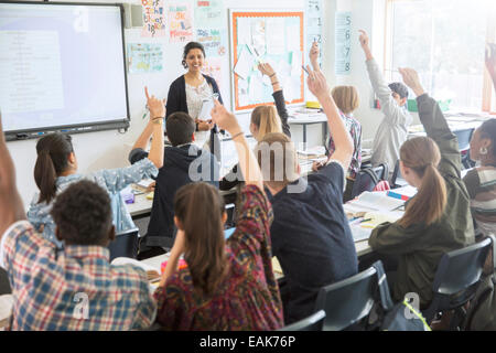 Vista posteriore di adolescenti studenti alzando le mani in aula Foto Stock