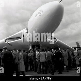 Degli anni Cinquanta, storiche, i membri della stampa si radunano all'esterno al di sotto della cabina di pilotaggio del nuovo caccia jet-powered ala delta bombardiere strategico, l'Avro Vulcan B.2, in corrispondenza del suo lancio stampa, Inghilterra, Regno Unito. Foto Stock