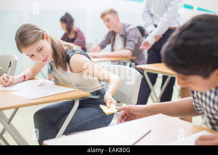 Gli studenti passando nota tra le scrivanie durante i loro esami GCSE Foto Stock