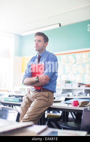 Ritratto di insegnante maschio appoggiata alla scrivania in aula Foto Stock