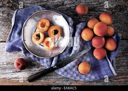 Fresche albicocche su una piastra di stagno con un coltello da cucina e asciugamani su uno sfondo di legno Foto Stock
