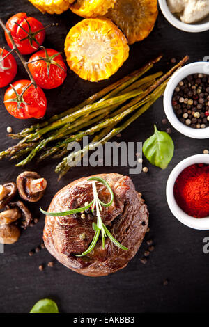 Pezzo di carne rossa di manzo con verdure, erbe e spezie, servito su pietra nera superficie. Scattato dalla vista superiore Foto Stock