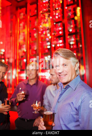 Ritratto di sorridere uomo maturo di contenimento di vetro di birra in discoteca, amici in background Foto Stock