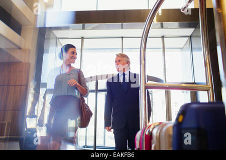 Uomo sorridente e la donna entrando in hotel lobby, valigie sul carrello portabagagli in primo piano Foto Stock