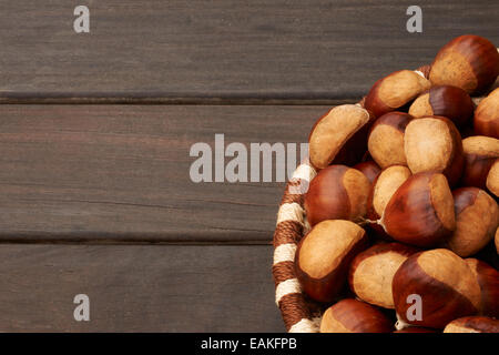 Cestello di grandi castagne al buio su un tavolo di legno Foto Stock