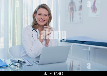 Ritratto di donna sorridente medico seduto alla scrivania con computer portatile Foto Stock