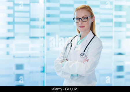 Ritratto di donna sorridente medico indossando occhiali e camice in piedi con le braccia incrociate Foto Stock