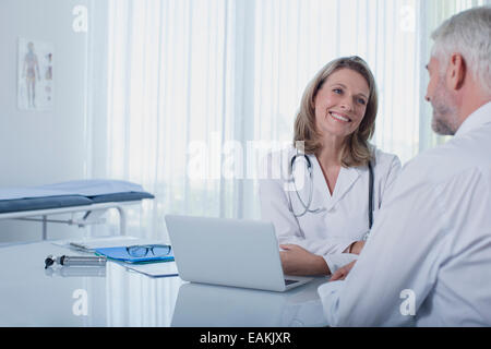 Donna sorridente medico parlando al paziente alla scrivania in ufficio Foto Stock