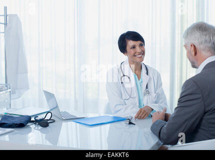 Donna sorridente medico parlando al paziente alla scrivania in ufficio Foto Stock