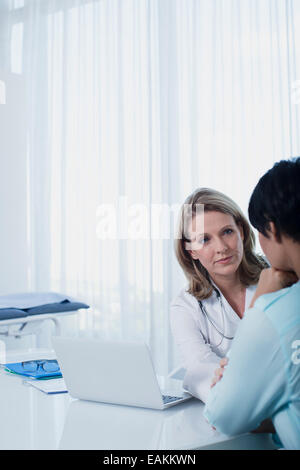 Medico donna parlando di donna alla scrivania in ufficio Foto Stock