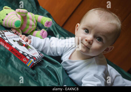 Una bambina (ca. 7 mesi di età) legge un bambini prenota. Foto Stock