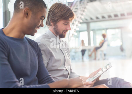 Due imprenditori sorridente con tavoletta digitale in ufficio Foto Stock