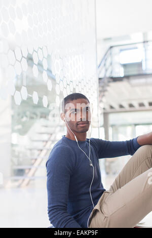 Uomo che ascolta musica in cuffia, seduto sul pavimento nel corridoio di office Foto Stock