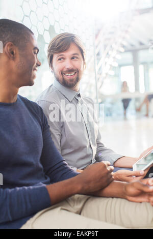 Due uomini sorridenti parlando, tenendo digitale compressa nel corridoio di office Foto Stock