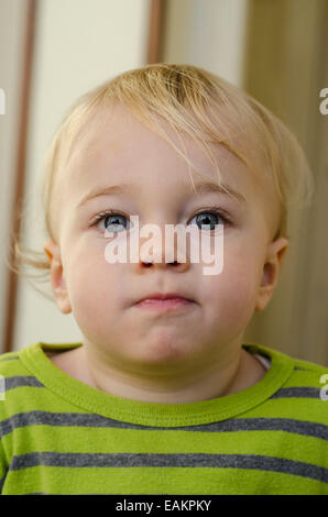 Un cheeky-cercando bionda e blue-eyed baby boy (ca. Diciotto mesi di età). Foto Stock