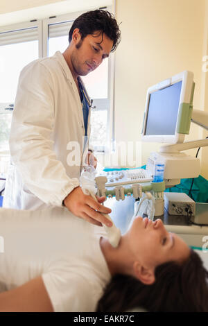 Un bel medico utilizzando una macchina ad ultrasuoni sulla gola di una giovane ragazza Foto Stock