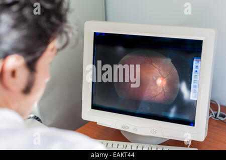 Un giovane oculista guardando una scansione della retina in un monitor di un computer Foto Stock