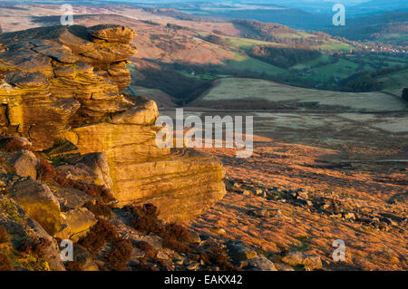 Vista dal bordo Stanage al tramonto con il bagliore dorato su gritstone rocce. Villaggio di Hathersage in distanza. Foto Stock