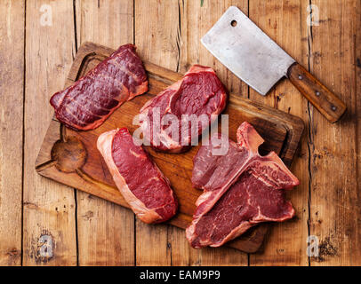 Diversi tipi di materie carni fresche bistecche e carne cleaver sul bordo di taglio su sfondo di legno Foto Stock