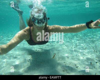 Nuotatore femmina indossando maschera e pinne soffiando bolle di aria nella subacquea ocean su fondo sabbioso Foto Stock