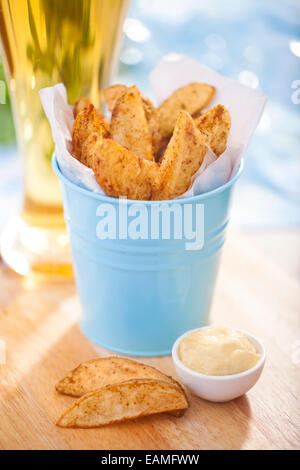 Spicchi di patate in un secchio con un bicchiere di birra Foto Stock